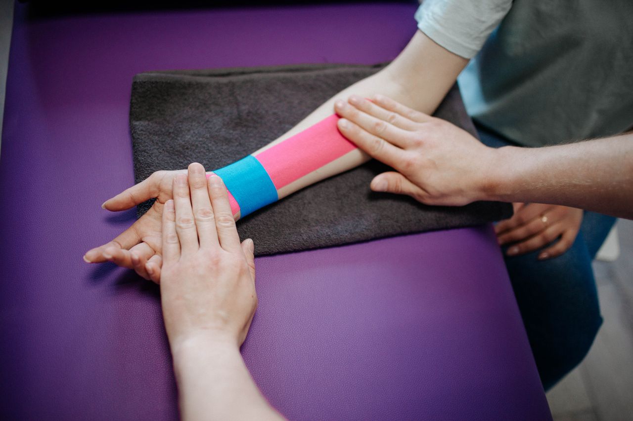 Home A therapist carefully applying colorful kinesiology tape on a patient's forearm for supportive therapy.